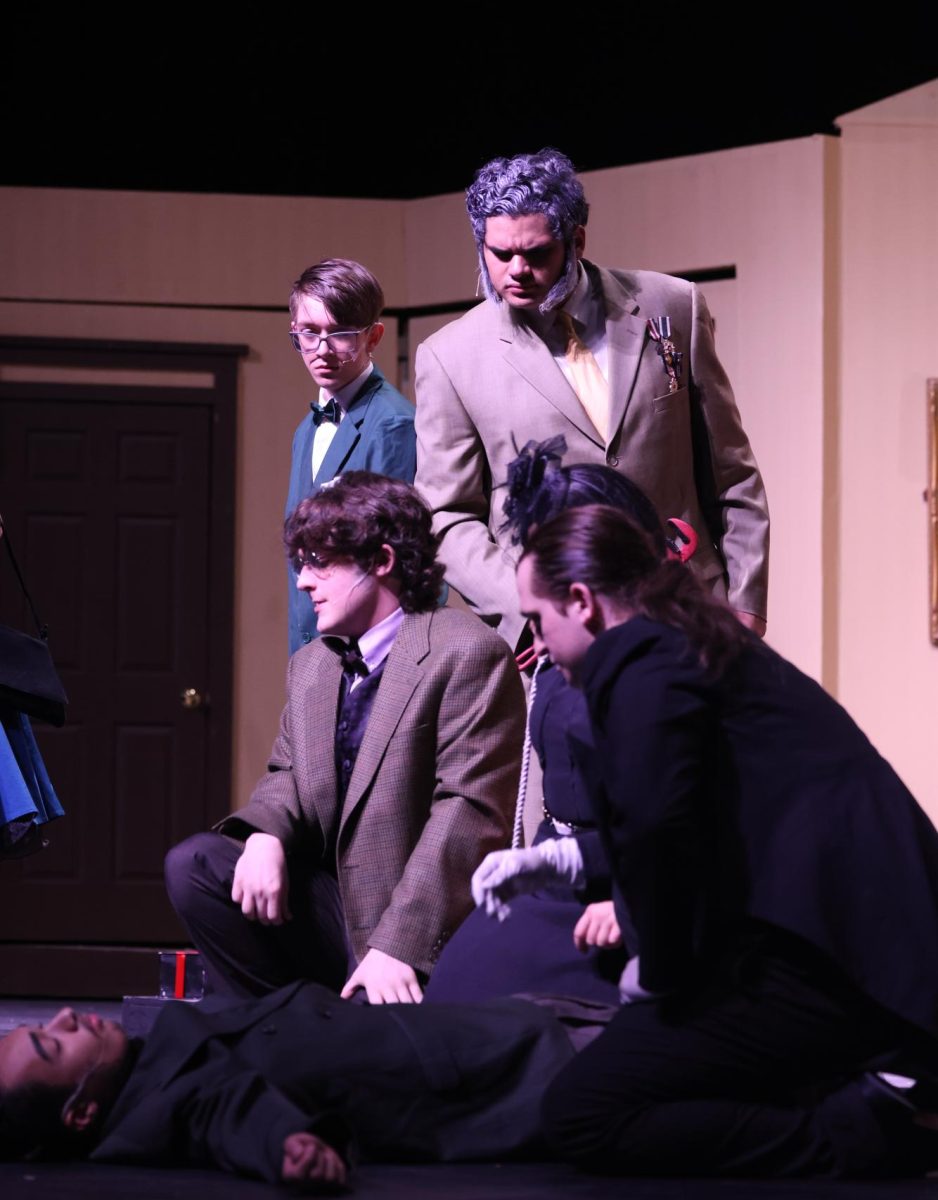 Mr.Green, played by Gavin DeGroot, and the Colonel played by Henry Patino, observe the host, Mr. Body, on the ground after his untimely death. 