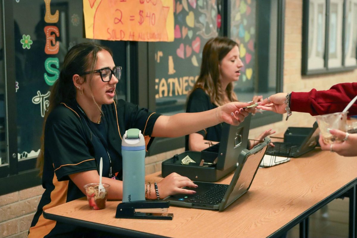 Exchanging money for carnival tickets, Student Council members, senior Emma Zirar and sophomore Rae Barber, work quickly so the student buyer can get to the activities in the commons.
